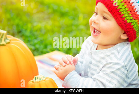 Closeup portrait of a nice cheerful baby boy de rire et de profiter de temps prévues à l'extérieur, assis près de deux citrouilles, symbole traditionnel de thanksgivi Banque D'Images