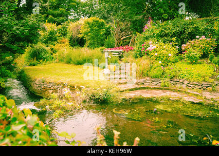 Étapes menant de ruisseau en bas du jardin pour borne fontaine entourée de fleurs et d'arbres dans un jardin de style informel Banque D'Images