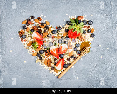 Ingrédients pour la cuisson petit déjeuner sain en forme de coeur. fraises, bleuets, écrous, des flocons d'avoine, fruits secs, miel avec drizzlier sur con Banque D'Images