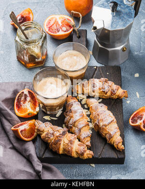 Petit-déjeuner de style italien accueil. latte, amande croissants et sanglant rouge sur les oranges en bois servant au tableau texturé en béton, moka Banque D'Images