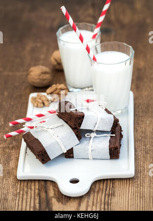 Tranches de chocolat enveloppé dans du papier et fatigué avec corde, verres de lait, les pailles, les noix sur une bande en céramique blanche en bois rustique au conseil backg Banque D'Images