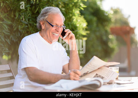 Homme caucasien parlant sur téléphone cellulaire et lisant des journaux Banque D'Images