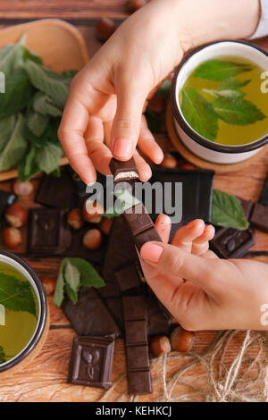 Mains de la femme cassant le chocolat près du thé vert Banque D'Images