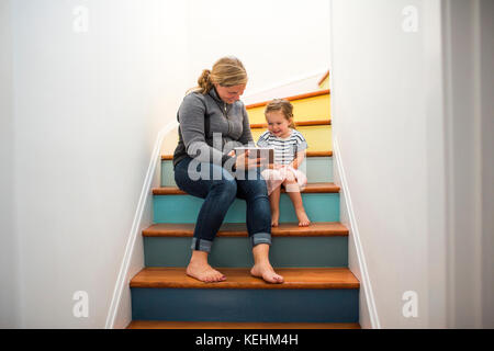 Mère et fille caucasiennes utilisant une tablette numérique sur l'escalier Banque D'Images