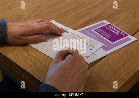 View of man's hands remplissant uk formulaire de demande de passeport sur table avec livret pédagogique Banque D'Images