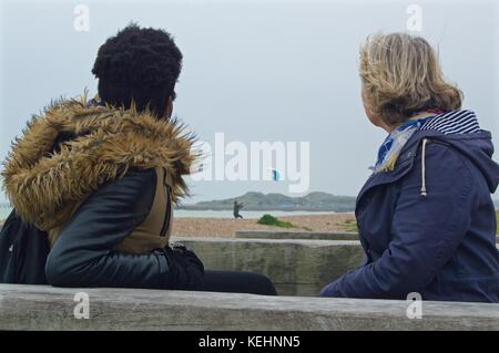 Deux dames regardant un homme voler un cerf-volant au bord de la mer, Littlehampton, Royaume-Uni Banque D'Images