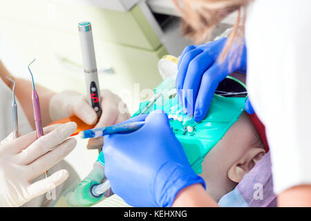 Close-up of a female dentist dans un sarrau blanc et un chapeau médicaux stériles L'inspection des dents pour la carie et la plaque à un enfant, le dentiste assista Banque D'Images