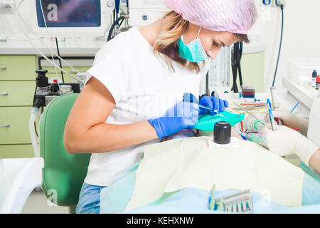 Une belle jeune femme dentiste dans un sarrau blanc et un chapeau médicaux stériles vérifie ses dents pour la carie et la plaque à un enfant, le dentiste assi Banque D'Images