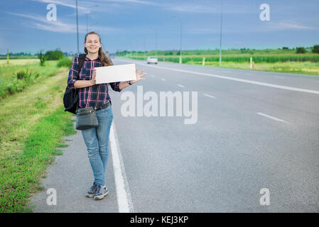 Smiling woman auto-stoppeur sur la route est holding a blank board. concept : voyager à travers le monde, d'euros, les vacances, les gens, les vacances. Banque D'Images