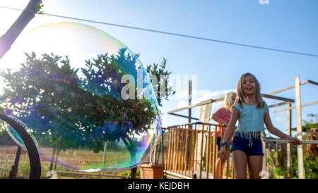 Jeune fille fait une bulle de savon alors que d'autres enfants excités regarder et attendre leur tour Banque D'Images