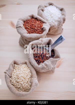 Grains entiers mixtes riz riz thaï traditionnel meilleur pour la santé des aliments et super dans le chanvre sac sacs setup sur fond de bois. Banque D'Images