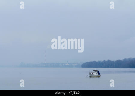 Belgrade sous le brouillard vu de Zemun, avec un bateau à l'avant, sur le Danube, et les fumées d'une cheminée industrielle dans l'arrière-plan photo o Banque D'Images