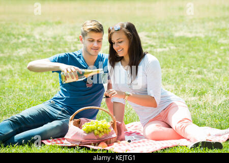 Young man pouring champagne en verre pour happy woman at park Banque D'Images