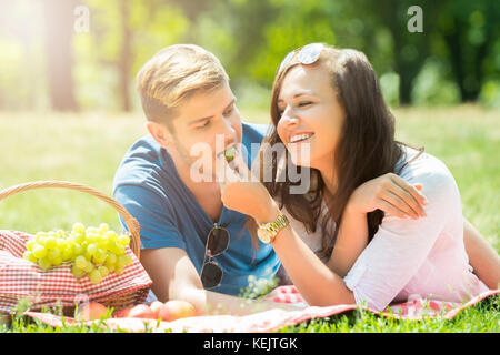 Smiling young woman feeding raisin à son petit ami en park Banque D'Images