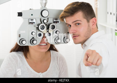 Jeune homme ophtalmologiste avec femme à phoropter pour essai d'oeil Banque D'Images