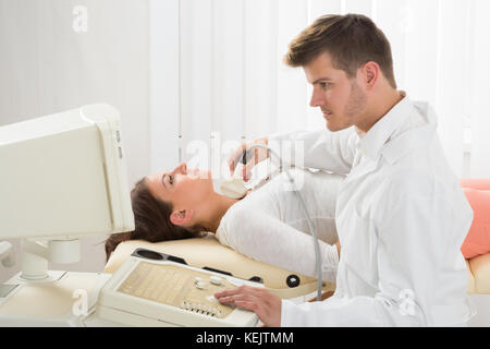 Un beau médecin à l'aide d'un appareil à échographie sur la gorge d'une patiente Banque D'Images