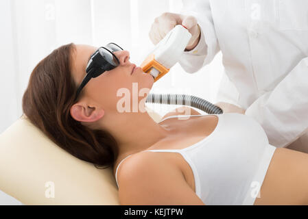 Close-up of Smiling Young Woman Having Traitement au laser à la Clinique de beauté sur le visage Banque D'Images