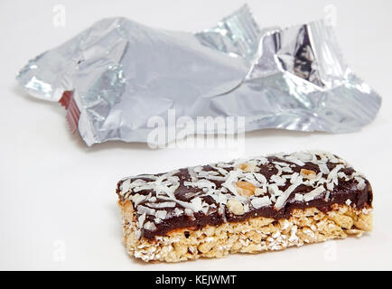 Barre granola garnies de noix de coco et chocolat sur fond blanc d'une feuille d'emballage dans l'arrière-plan. L'accent sur le premier plan barre granola. Banque D'Images