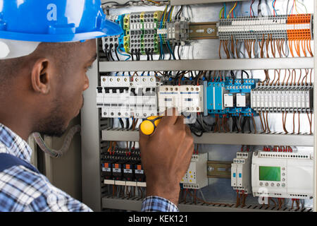 Close-up of young male technician l'examen de la boîte à fusibles avec tournevis Banque D'Images