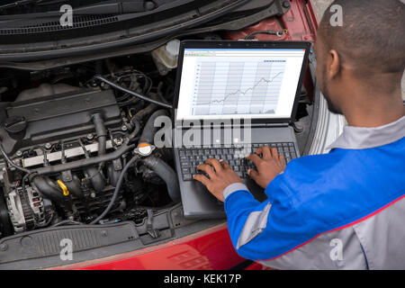 Mécanicien de jeunes hommes à l'aide d'ordinateur portable lors de l'examen du moteur de voiture Banque D'Images