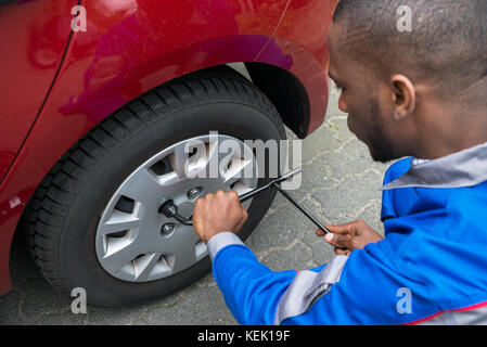 Jeune Mécanicien africain changer pneu d'une voiture rouge avec une clé Banque D'Images