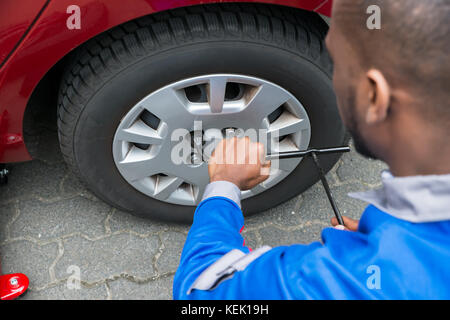 Jeune Mécanicien africain changer pneu d'une voiture rouge avec une clé Banque D'Images