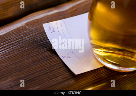 Vue rapprochée d'un verre de bière avec un bill allongé sur une table dans une taverne Banque D'Images