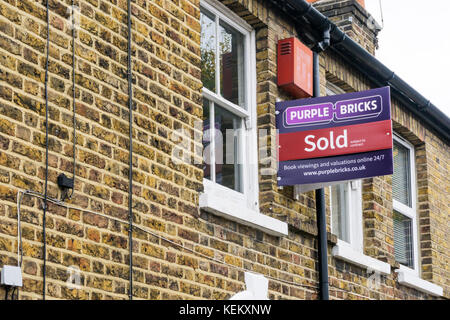 Un signe sur une maison vendue par des agents immobiliers en ligne briques violet Banque D'Images