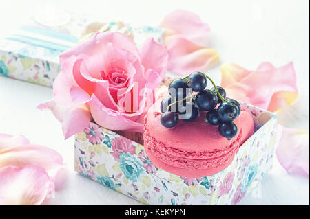 Macarons aux groseilles dans une boîte-cadeau sur l'arrière-plan de belles fleurs roses. Dessert close-up. La structure horizontale. Banque D'Images