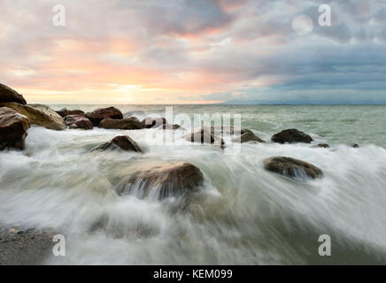 Les vagues de l'océan lune coucher du soleil est un paysage marin abstrait surréaliste avec des vagues se précipiter sur les rochers, alors que le soleil se couche sur l'horizon de l'océan et la lune se lève dans le sk Banque D'Images