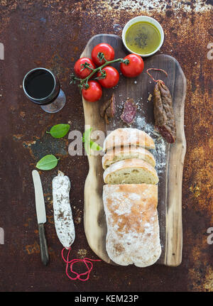 Pain ciabatta fraîchement cuits au four avec tomates-cerises, de salami, de pesto, le basilic et le verre de vin rouge sur bois de noix sur grunge métal rouillé backg Banque D'Images