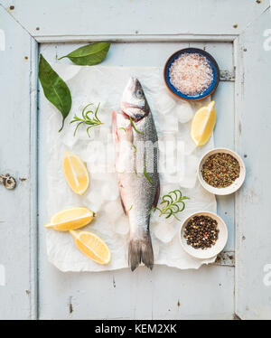 Crus frais poissons bar méditerranéen avec du citron, des herbes, de la glace et les épices sur fond bleu rustique de bois, vue du dessus Banque D'Images