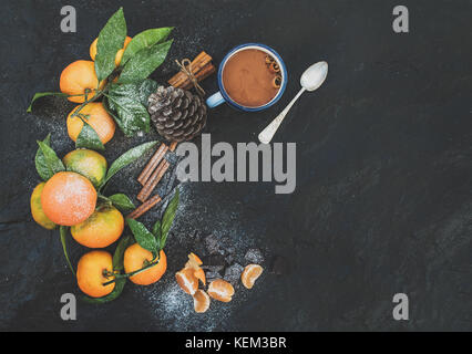 Noël ou Nouvel an. cadre des mandarines fraîches avec des feuilles, des bâtons de cannelle, vanille, pomme de pin et de tasse de chocolat chaud sur fond de pierre sombre, Banque D'Images