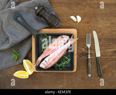 Rouget cru cru poisson dans une casserole avec le romarin, le citron et l'ail sur fond de bois rustique, vue du dessus Banque D'Images