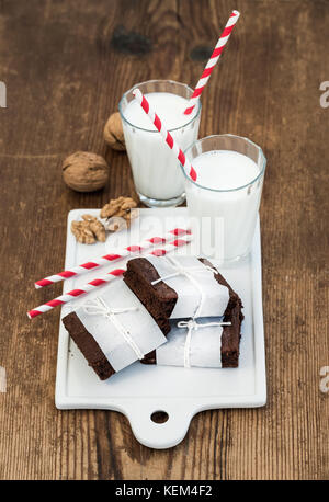 Tranches de chocolat enveloppé dans du papier et fatigué avec corde, verres de lait, de pailles, de noix sur conseil de céramique blanche sur fond de bois rustique Banque D'Images