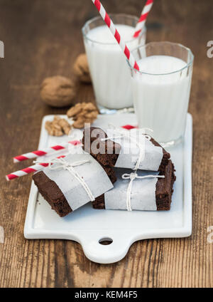 Tranches de chocolat enveloppé dans du papier et fatigué avec corde, verres de lait, de pailles, de noix sur conseil de céramique blanche sur fond de bois rustique Banque D'Images