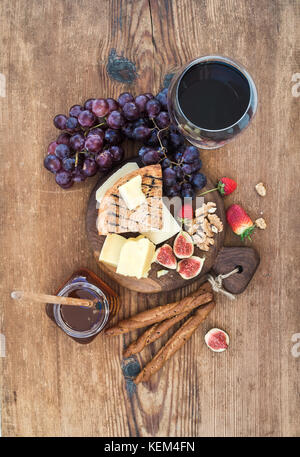 Verre de vin rouge, plateau de fromages, raisins,fig, fraises, miel et bâtonnets de pain sur table en bois rustique Banque D'Images
