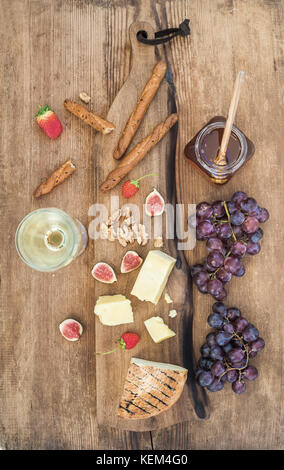 Verre de vin blanc, plateau de fromages, raisins, figues, fraises, miel et gressins sur fond de bois rustique Banque D'Images
