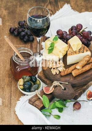 Verre de vin rouge, plateau de fromages, raisins,fig, fraises, miel et bâtonnets de pain sur table en bois rustique Banque D'Images