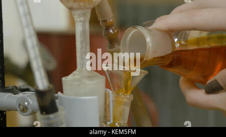 Verre chimique avec du liquide vert versé dans un rouge parmi les entonnoirs. La main ajoute le liquide mélangé rouge dans le flacon. un chimiste ou un chercheur médical ajoute des produits chimiques à un flacon erlenmeyer pour une réaction chimique Banque D'Images