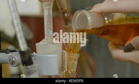 Verre chimique avec du liquide vert versé dans un rouge parmi les entonnoirs. La main ajoute le liquide mélangé rouge dans le flacon. un chimiste ou un chercheur médical ajoute des produits chimiques à un flacon erlenmeyer pour une réaction chimique Banque D'Images