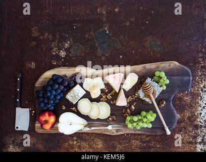 Hors-d'vin set : sélection de fromages français, de miel, de raisin, de pêche et de noix sur planche de bois rustique sur dark grunge metal background. Vue de dessus Banque D'Images