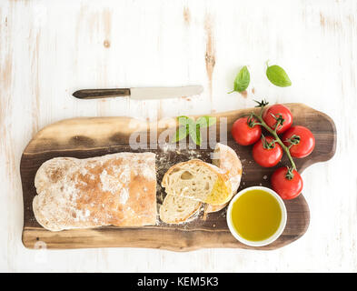 Pain ciabatta fraîchement cuits au four avec tomates-cerises, de l'huile d'olive, le basilic et le sel sur bois sur fond blanc, vue du dessus Banque D'Images