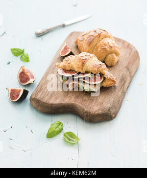 Des croissants frais avec des figues fraîches et prosciutto sur le service conseil au décor rustique en bois bleu Banque D'Images