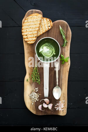 Vert maison crème d'épinards-soupe dans un metal scoop avec les tranches de pain grillé, d'herbes, d'épices en bois rustique sur fond noir au cours du conseil Banque D'Images