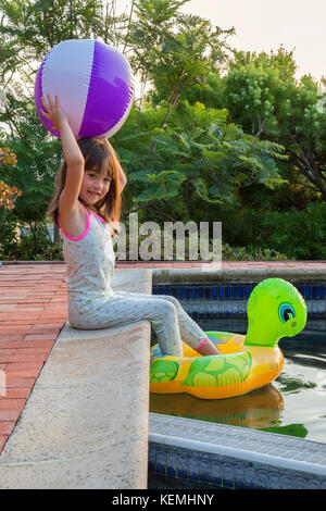 Jeune fille assise au bord de la piscine tout en tenant une balle