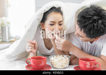 Les jeunes couples asiatiques de prendre le petit déjeuner sur le même lit dans la chambre de maison contemporaine de style moderne concept Banque D'Images