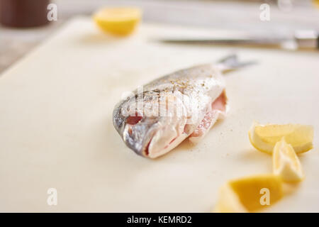 Le poisson cru avec des épices et du citron. Le poisson frais avec le citron sur une planche à découper. la cuisson du poisson dorado. Banque D'Images