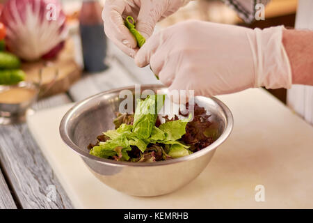 Les mains du chef chopping laitue. vert et violet feuilles de laitue dans un bol en acier inoxydable. chef au travail, cuisine. Banque D'Images