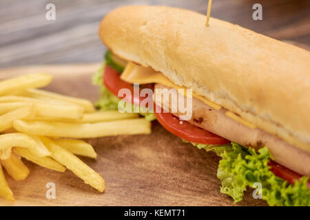 De délicieux hot-dog et frites. appétissant hot dog avec laitue, tomates, concombres, fromage, saucisse de poulet sur fond de bois. Banque D'Images